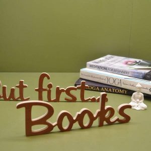 Medinis pastatomas užrašas "But first...Books"
